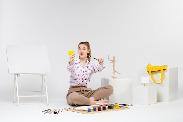 Vue de face jeune femme tenant une carte bancaire jaune sur fond blanc