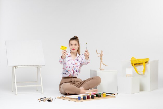 Vue de face jeune femme tenant une carte bancaire jaune sur fond blanc