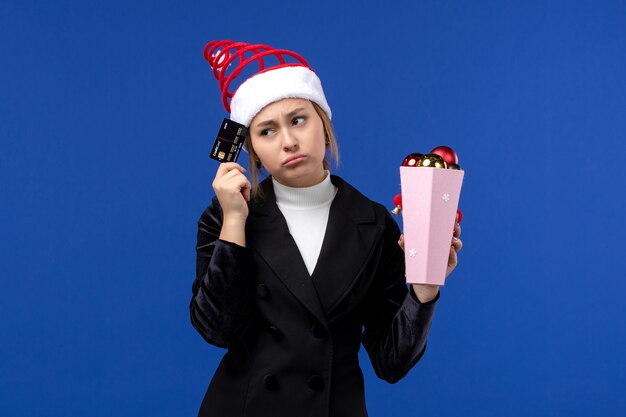 Vue de face jeune femme tenant une carte bancaire sur mur bleu vacances nouvel an émotion
