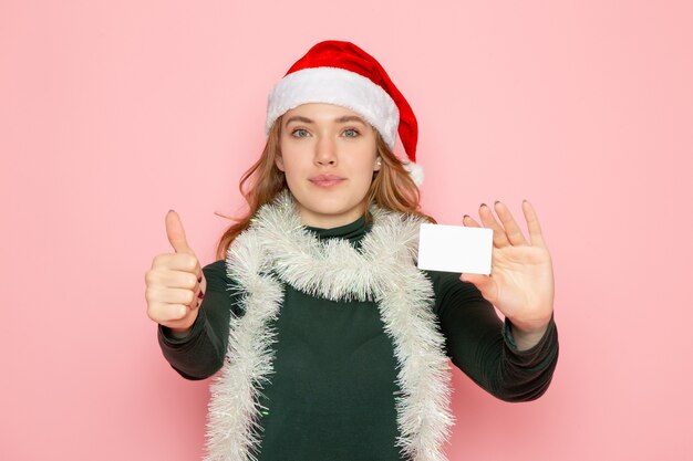 Vue de face jeune femme tenant une carte bancaire sur le mur rose couleur modèle vacances Noël nouvel an émotion