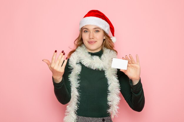 Vue de face jeune femme tenant une carte bancaire sur le mur rose couleur modèle vacances Noël nouvel an émotions