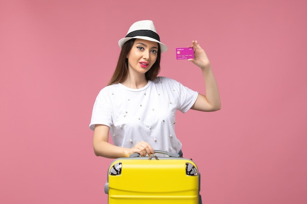 Vue de face jeune femme tenant une carte bancaire sur le mur rose voyage vacances femme argent