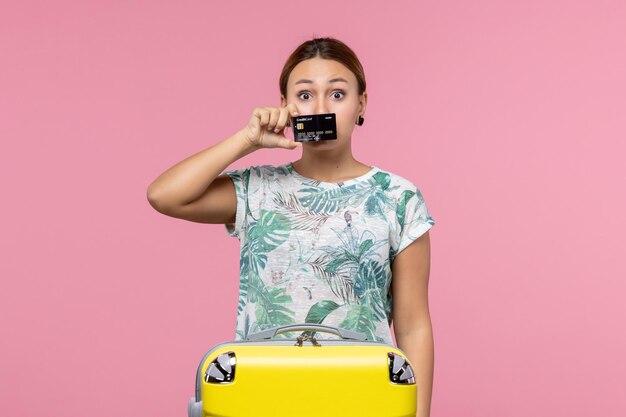 Vue de face d'une jeune femme tenant une carte bancaire noire sur le mur rose