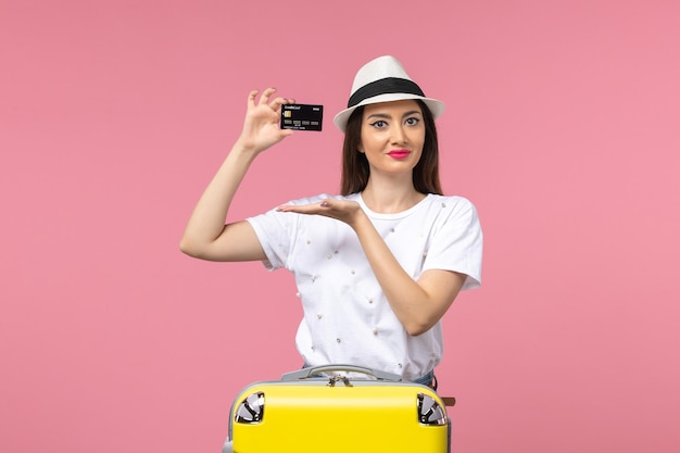 Vue de face jeune femme tenant une carte bancaire noire sur un voyage de couleur de voyage de mur rose