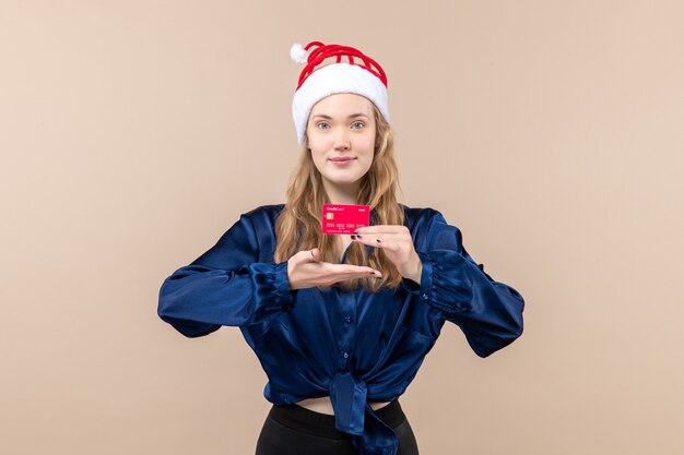 Vue de face jeune femme tenant une carte bancaire rouge sur fond rose vacances photo nouvel an émotion argent de Noël