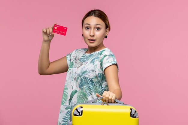 Vue de face jeune femme tenant une carte bancaire rouge sur un mur rose vol voyage avion reste femme