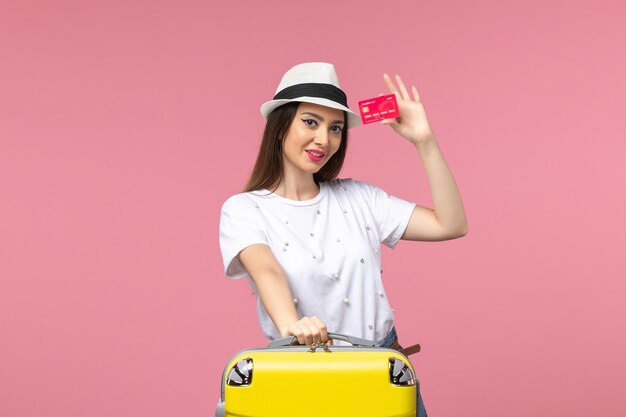 Vue de face jeune femme tenant une carte bancaire rouge sur un voyage d'été de couleur de bureau rose