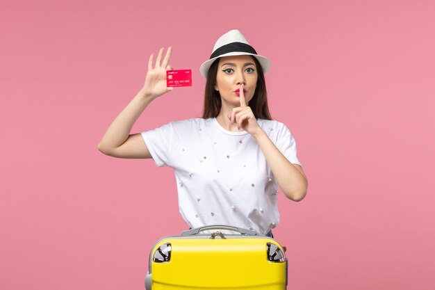 Vue de face jeune femme tenant une carte bancaire rouge sur un voyage d'été de voyage de bureau rose