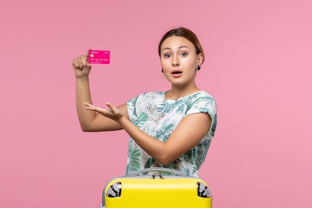 Vue de face jeune femme tenant une carte bancaire en vacances sur le mur rose été reste couleur voyage vacances femme