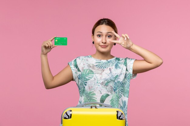 Vue de face jeune femme tenant une carte bancaire verte en vacances sur le mur rose voyage d'été vacances voyage reste femme