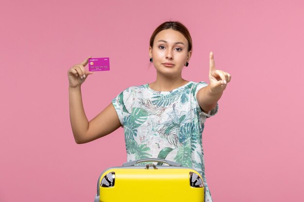 Vue de face jeune femme tenant une carte bancaire violette en vacances sur un mur rose clair couleur voyage vacances femme d'été