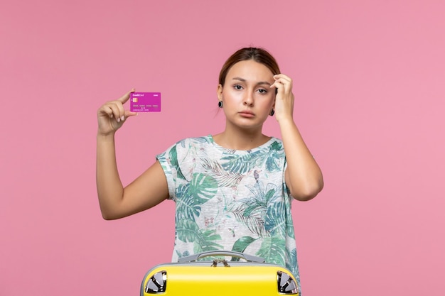 Vue de face jeune femme tenant une carte bancaire violette en vacances sur le mur rose couleur voyage vacances femme d'été