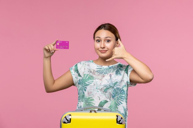 Vue de face jeune femme tenant une carte bancaire violette en vacances sur le mur rose voyage couleur vacances d'été femme