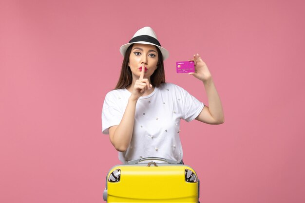 Vue de face jeune femme tenant une carte bancaire sur le voyage de femme d'argent de vacances de bureau rose