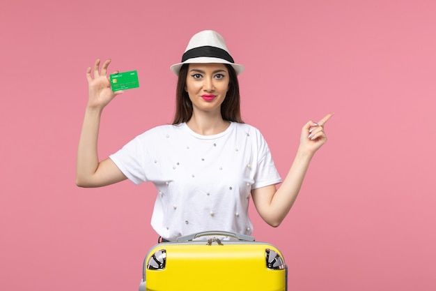 Vue de face jeune femme tenant une carte bancaire sur le voyage de femme d'été d'émotion de mur rose