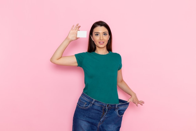 Vue de face jeune femme tenant une carte blanche sur mur rose exercice sport entraînement athlète taille beauté