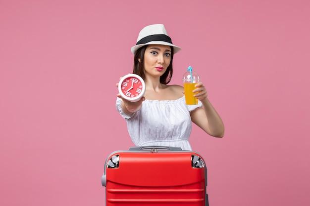 Vue de face jeune femme tenant un cocktail et une horloge en vacances sur un mur rose clair vacances chaleur voyage voyage été