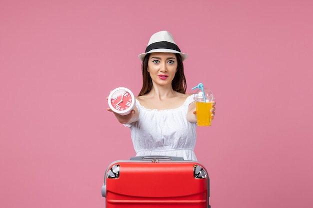 Vue de face jeune femme tenant un cocktail et une horloge en vacances sur un mur rose clair vacances couleur chaleur voyage voyage été