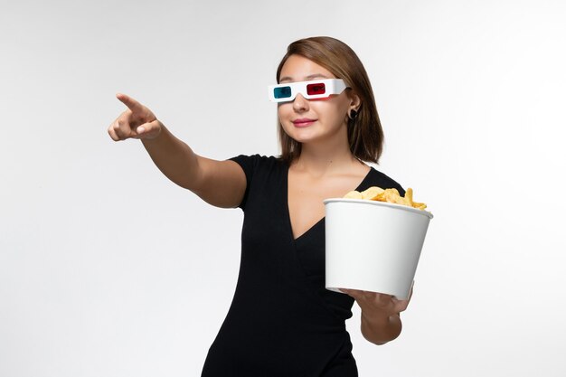 Vue de face jeune femme tenant des croustilles dans des lunettes de soleil et regarder un film sur une surface blanche