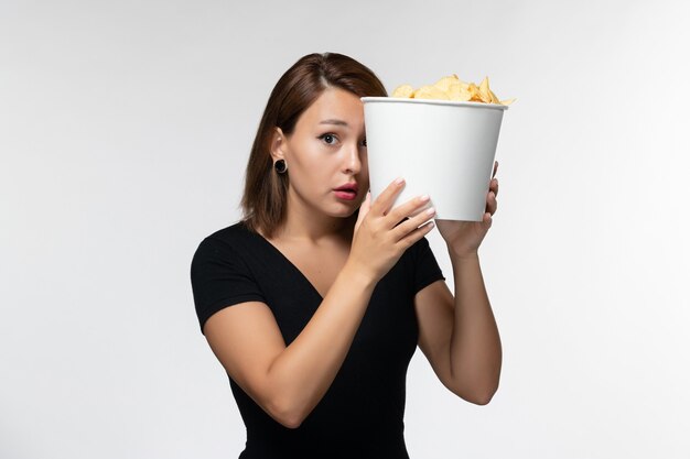 Vue de face jeune femme tenant des croustilles et regarder un film sur une surface blanche