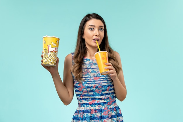 Vue de face jeune femme tenant du pop-corn et boire sur le bureau bleu
