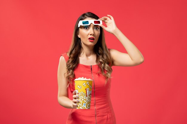Vue de face jeune femme tenant du pop-corn dans des lunettes de soleil sur le bureau rouge