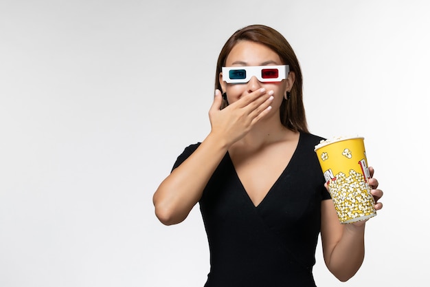 Photo gratuite vue de face jeune femme tenant du pop-corn dans des lunettes de soleil en regardant un film sur une surface blanche