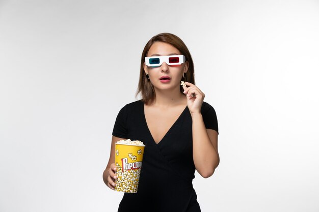 Vue de face jeune femme tenant du pop-corn dans des lunettes de soleil en regardant un film sur une surface blanche