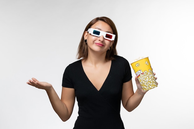 Vue de face jeune femme tenant du pop-corn en lunettes de soleil d regarder un film sur une surface blanche légère