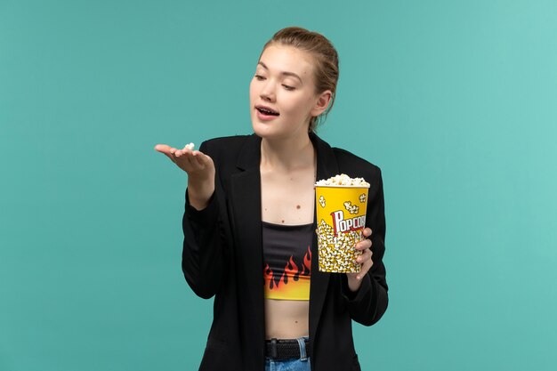 Vue de face jeune femme tenant du pop-corn et regarder un film sur un bureau bleu