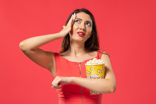 Vue de face jeune femme tenant du pop-corn sur la surface rouge