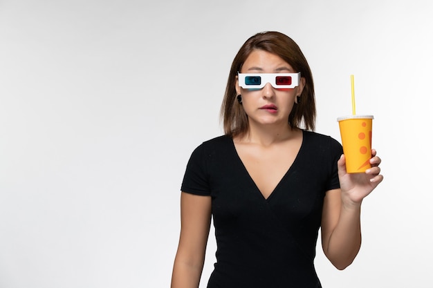 Vue de face jeune femme tenant du soda dans des lunettes de soleil sur une surface blanche légère