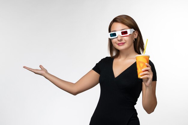 Vue de face jeune femme tenant du soda dans des lunettes de soleil sur une surface blanche