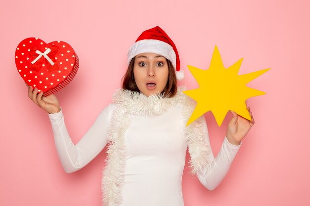 Vue de face jeune femme tenant la figure jaune et présente sur le mur rose de la neige de Noël couleur mode nouvel an