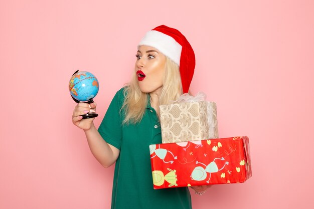 Vue de face jeune femme tenant globe et cadeaux de Noël sur le mur rose modèle photo femme Noël nouvel an vacances couleur