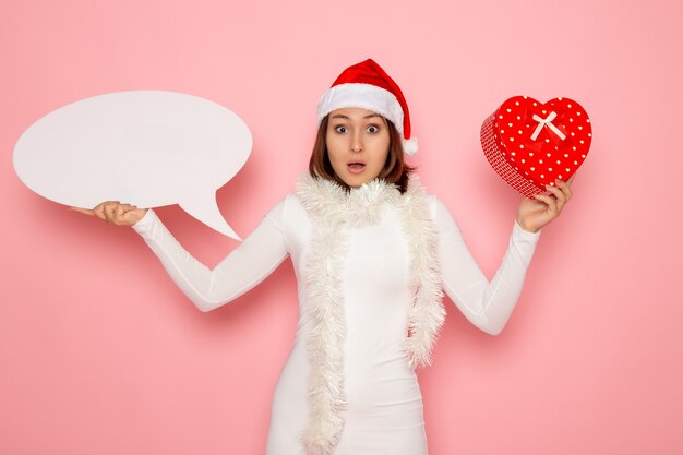 Vue de face jeune femme tenant grand panneau blanc et présent sur le mur rose couleur neige Noël nouvel an vacances d'émotion