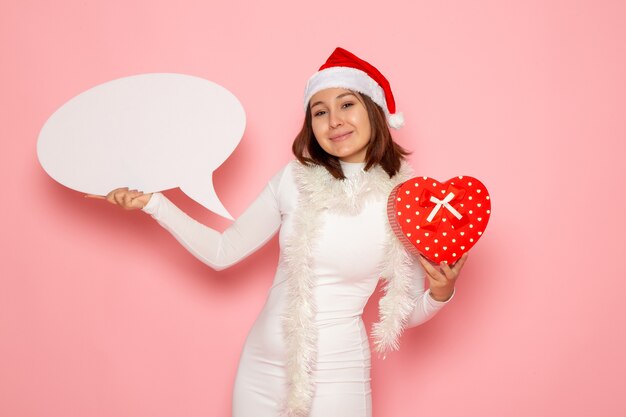 Vue de face jeune femme tenant grand panneau blanc et présent sur le mur rose neige Noël nouvel an vacances d'émotion