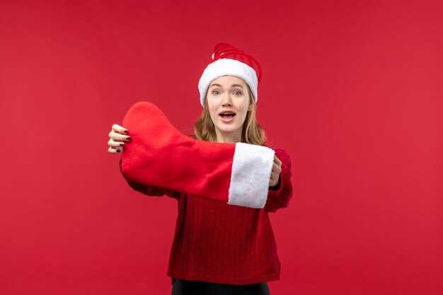Vue de face jeune femme tenant une grosse chaussette de noël sur un bureau rouge vacances noël rouge