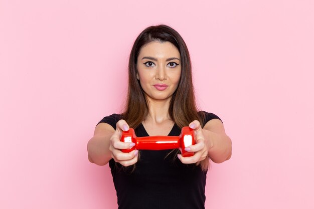 Vue de face jeune femme tenant des haltères sur le mur rose clair athlète sport exercice santé entraînement