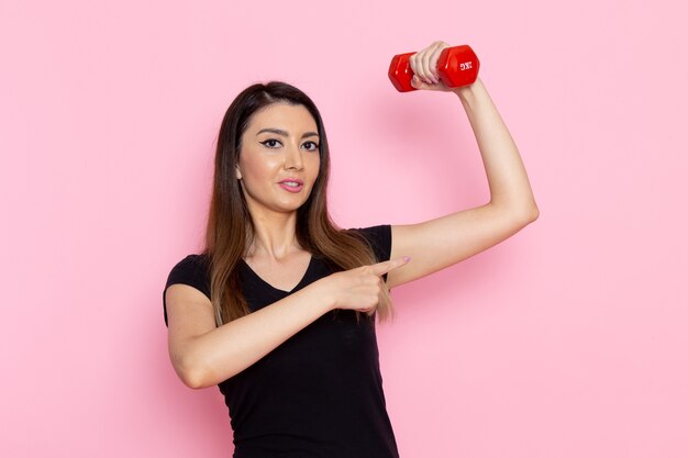 Vue de face jeune femme tenant des haltères sur le mur rose clair athlète sport exercice santé entraînement