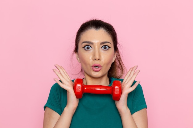 Vue de face jeune femme tenant des haltères rouges sur le mur rose athlète sport exercices de santé