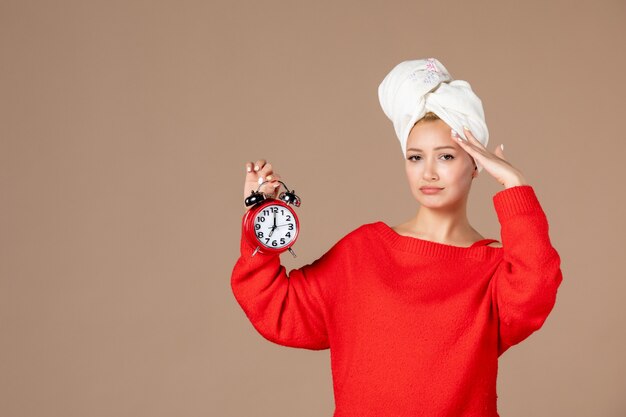 vue de face jeune femme tenant des horloges avec une serviette sur la tête sur un mur marron