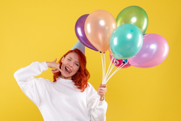 Vue de face de la jeune femme tenant de jolis ballons colorés sur mur jaune