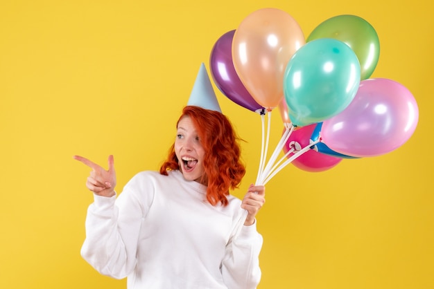 Vue de face de la jeune femme tenant de jolis ballons colorés sur mur jaune