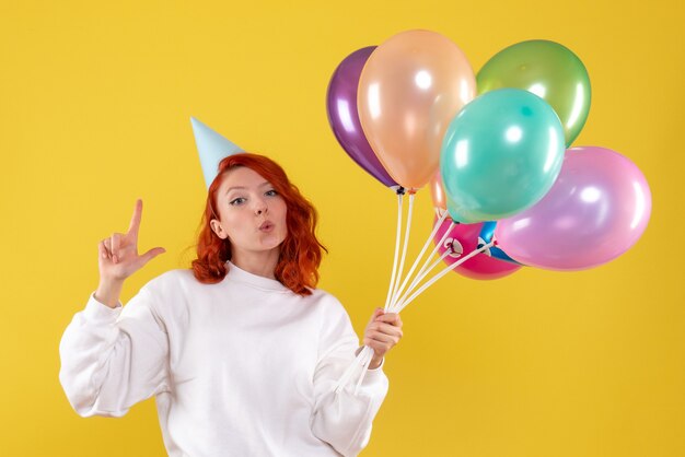 Vue de face de la jeune femme tenant de jolis ballons colorés sur mur jaune