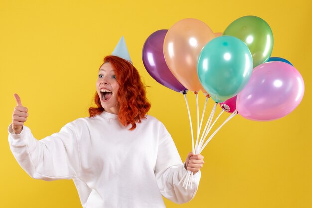 Vue de face de la jeune femme tenant de jolis ballons colorés sur mur jaune