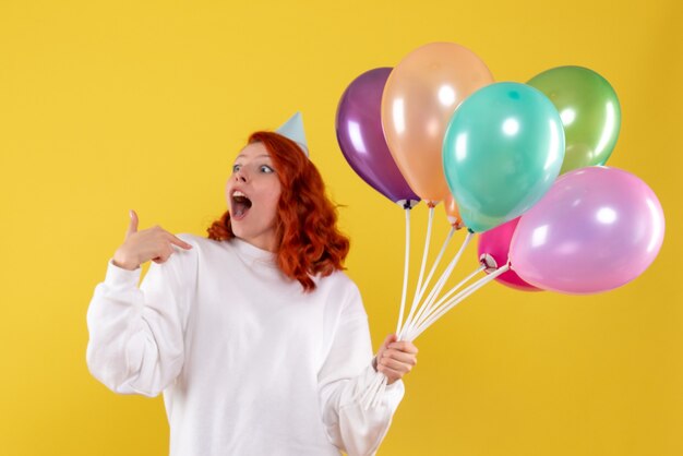 Vue de face de la jeune femme tenant de jolis ballons colorés sur mur jaune