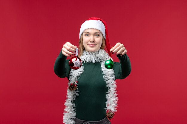 Vue de face jeune femme tenant des jouets d'arbre de Noël sur le fond rouge