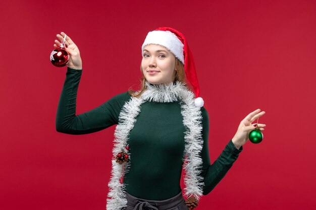 Vue de face jeune femme tenant des jouets d'arbre de Noël sur le fond rouge