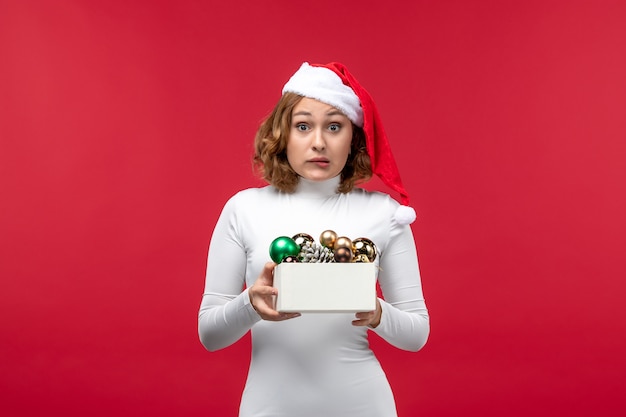 Vue de face de la jeune femme tenant des jouets de Noël sur rouge